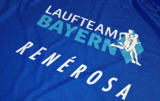 Die Logos von Laufteam Bayern und unserem Exklusivausrüster Renèrosa auf einem Raceshirt.